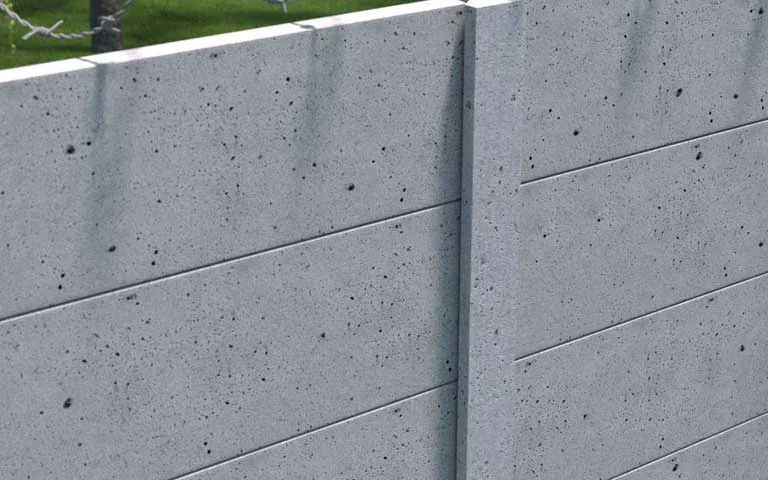 Grauer Industrie-Betonzaun mit glatten Zaunplatten und Stacheldraht darüber